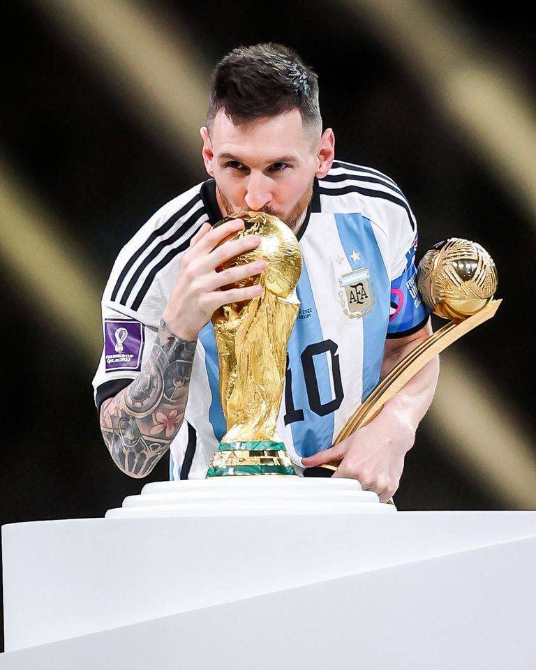 Messi kissing the World Cup trophy while holding the Golden Ball trophy